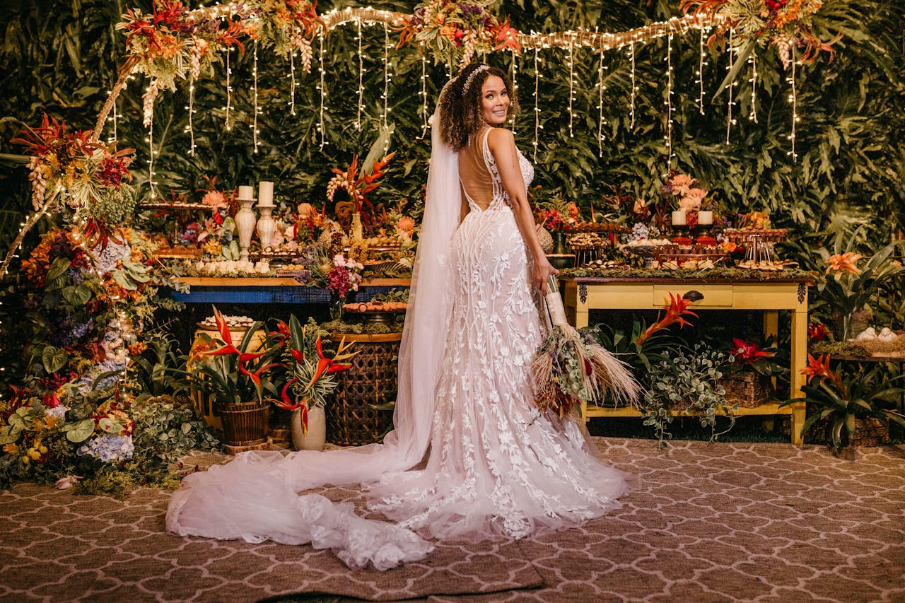A joyful bride in a floral wedding dress amidst lush tropical decor and vivid floral arrangements.