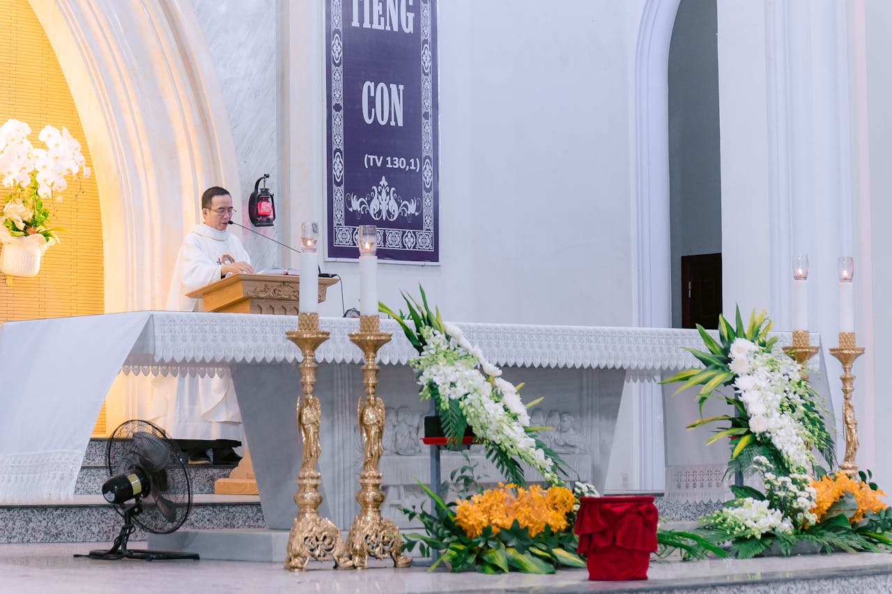 Priest delivering a sermon inside a beautifully decorated church with ornate details and floral arrangements.