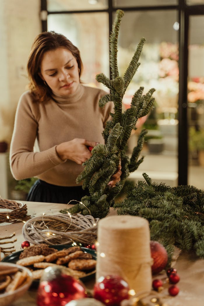 A woman arranging festive elements like pine branches and baubles on a table for holiday decor.